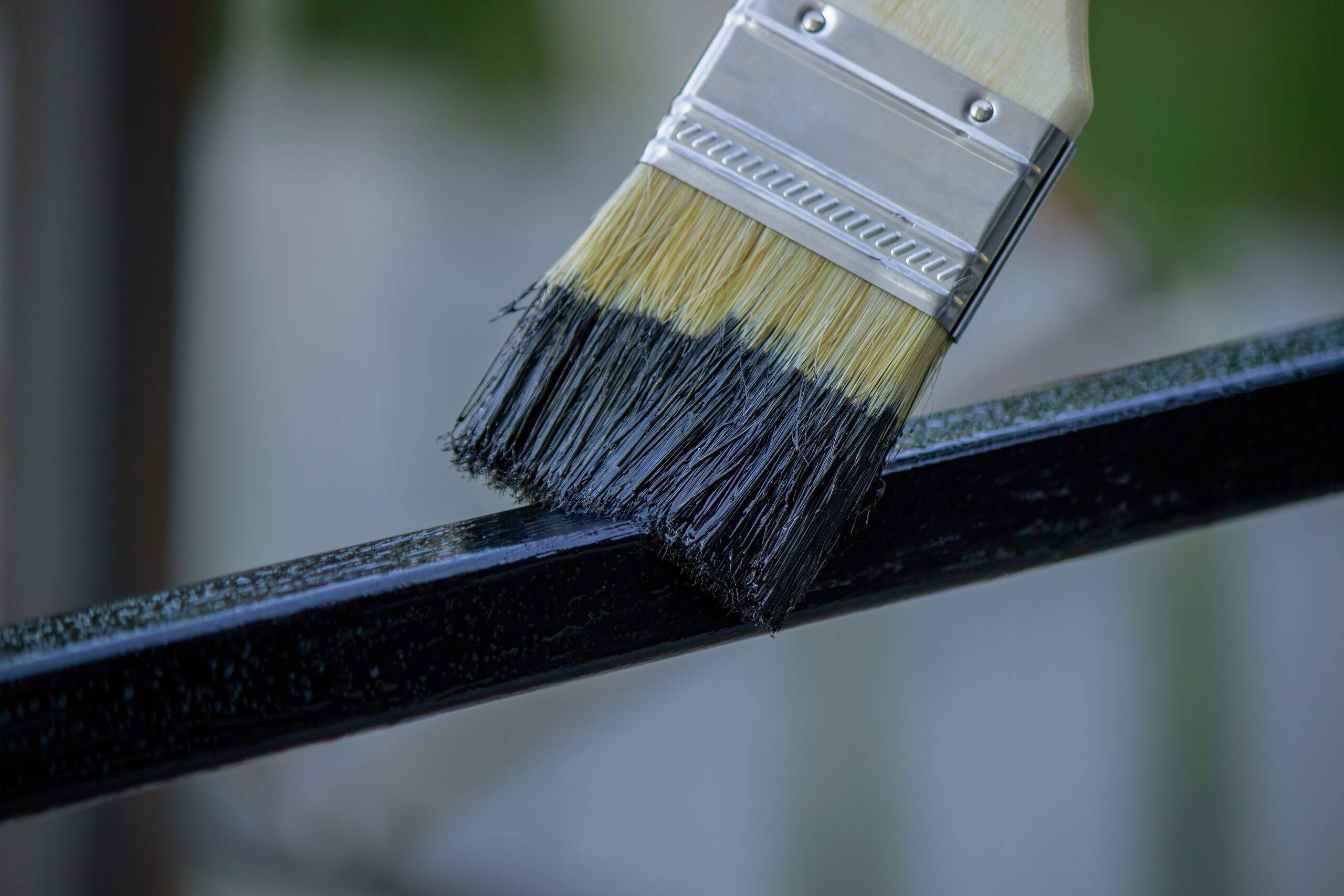 Brocha aplicando esmalte negro brillante sobre una barandilla metálica