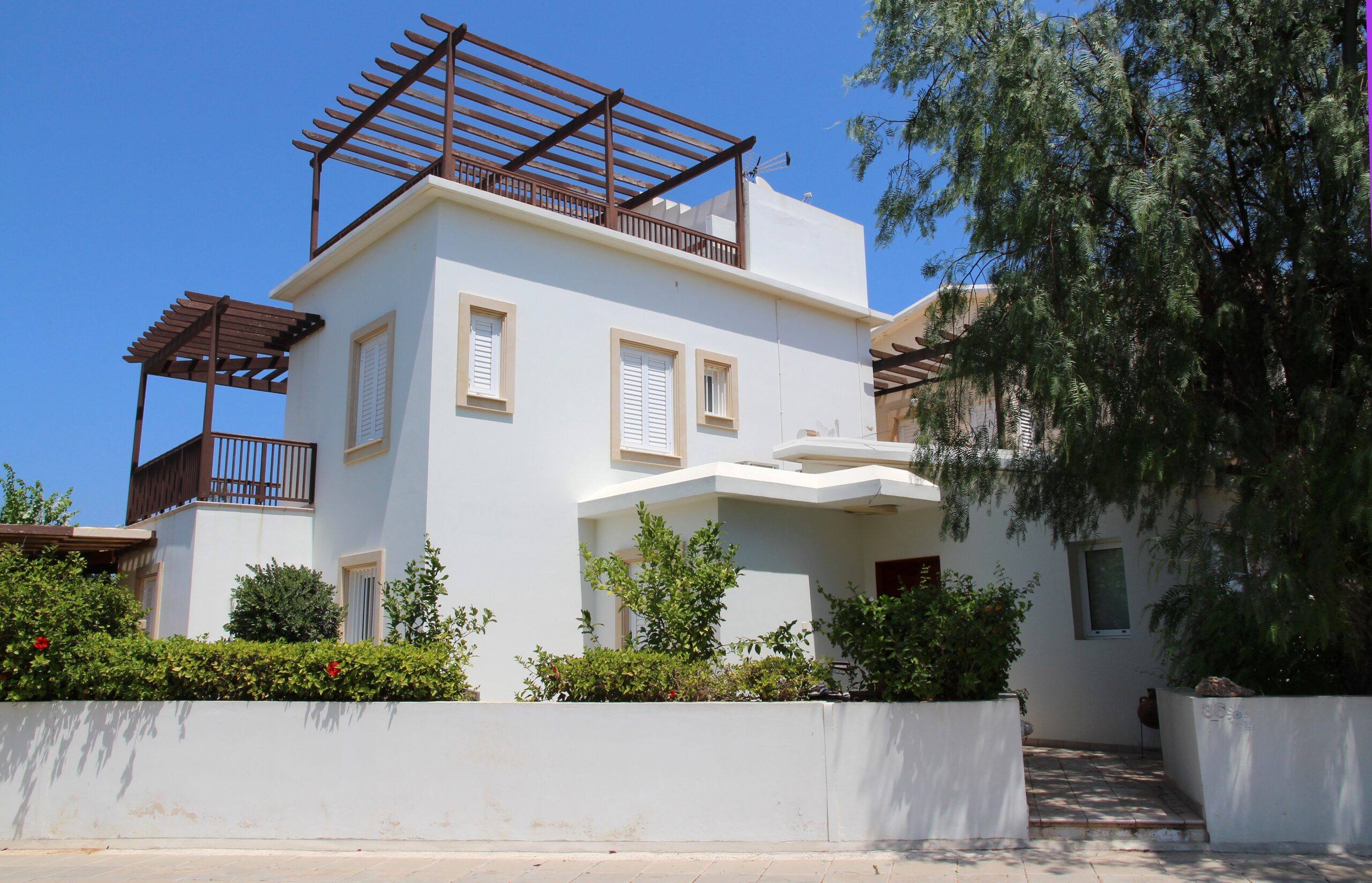Chalet blanco de estilo mediterráneo con pérgolas de madera y jardín bajo cielo azul