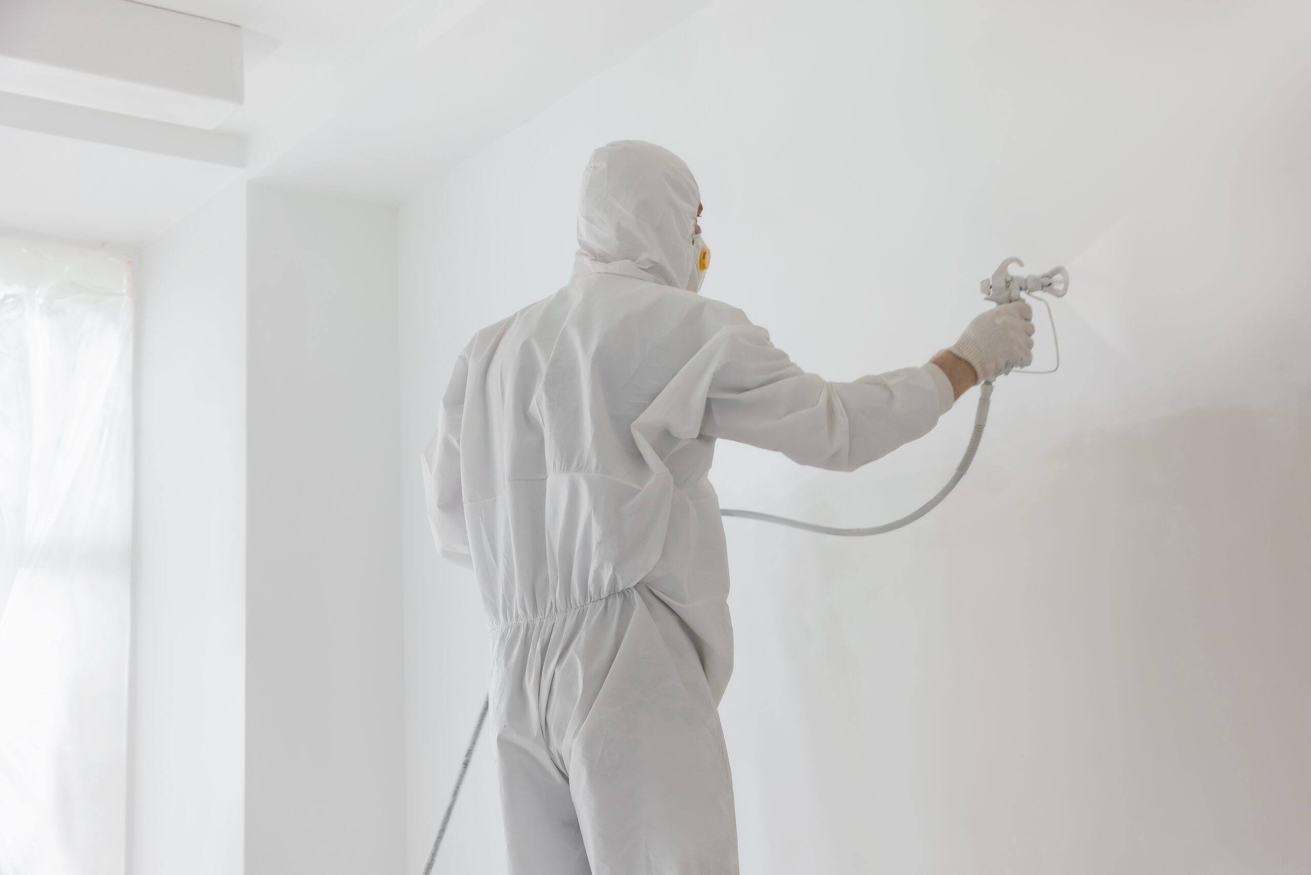 Pintor con mono blanco aplicando pintura con pistola airless