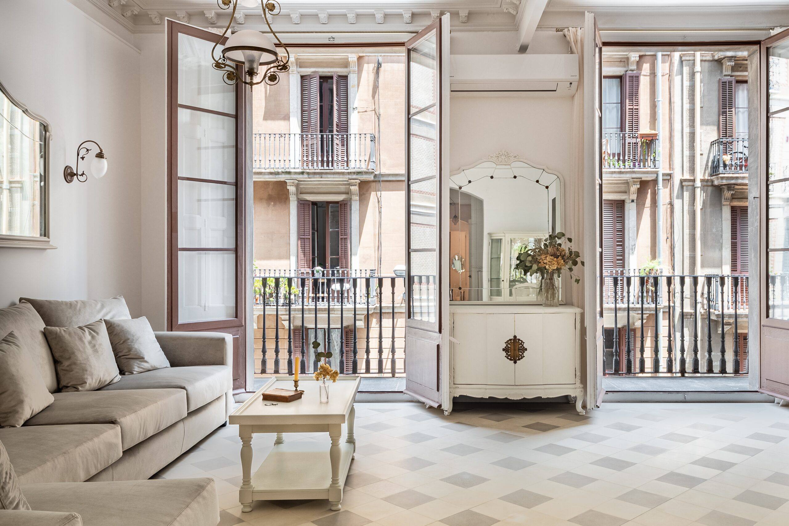 Salón luminoso de piso clásico con balcones de forja abiertos, sofá gris y suelo hidráulico