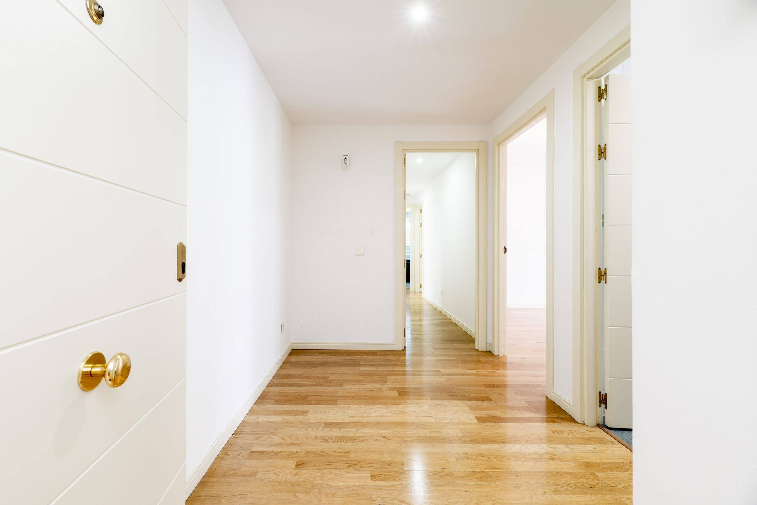 Pasillo de vivienda con puertas lacadas en blanco, pomos dorados y suelo de madera