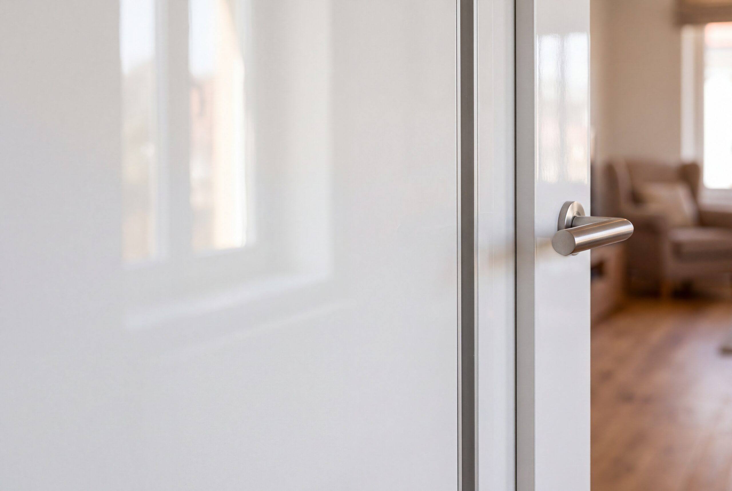 Detalle de una puerta lacada en blanco brillo con reflejo de la ventana y manilla de acero