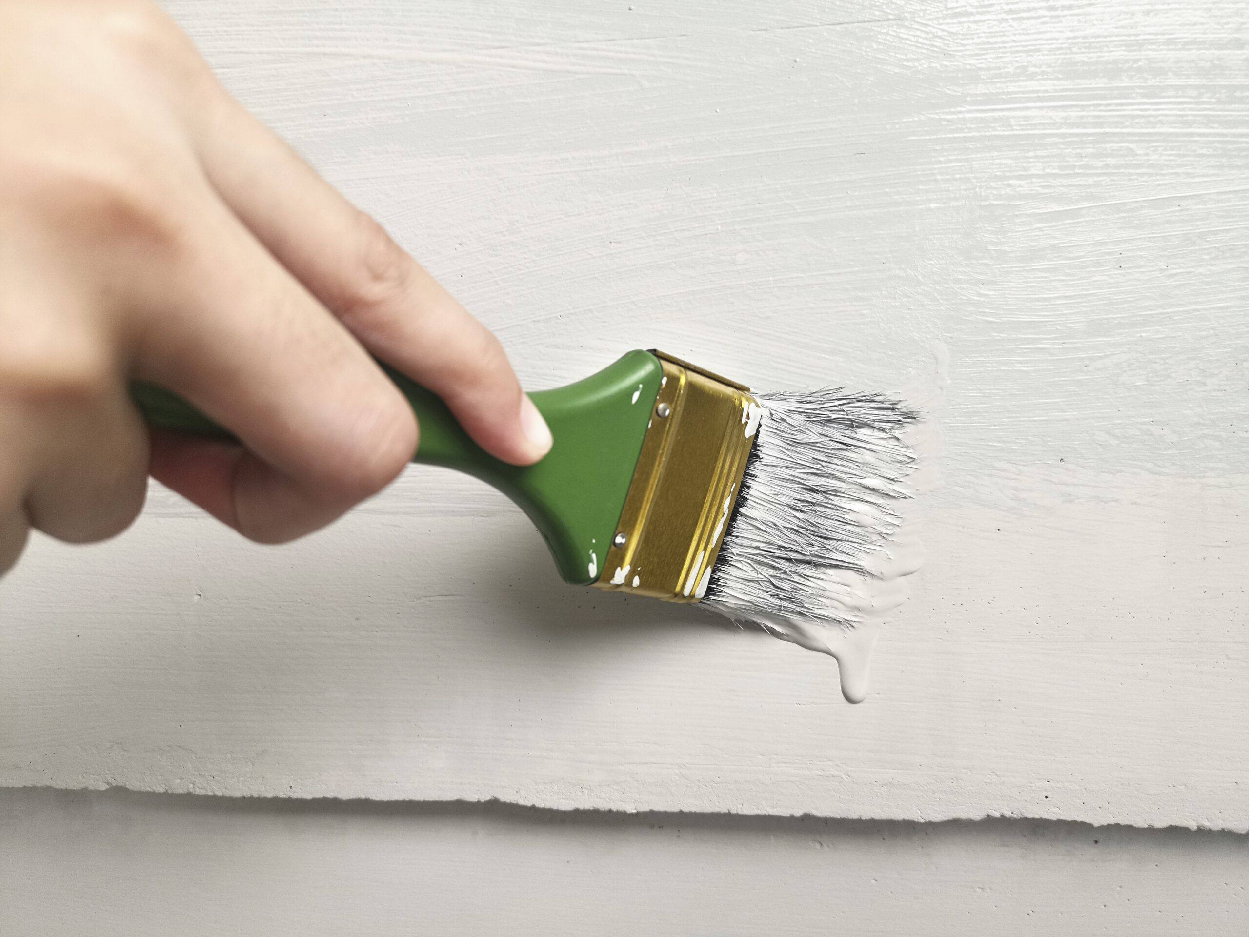 Mano retocando una pared blanca con una brocha cargada de pintura