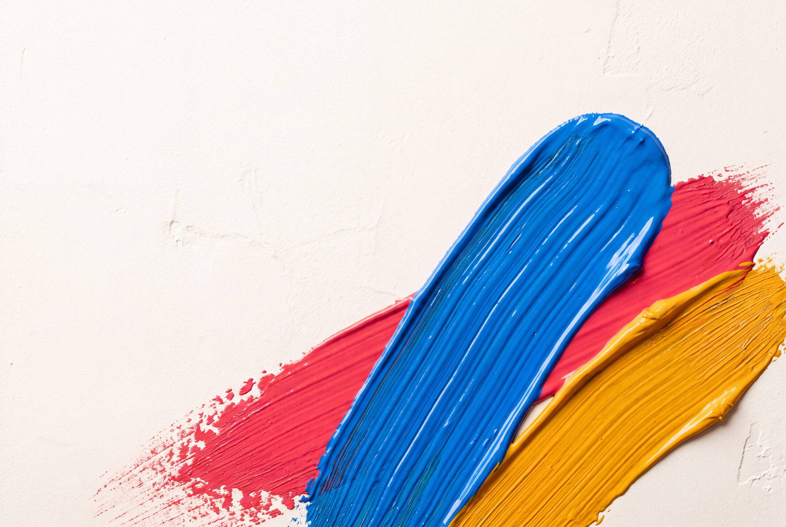 Pinceladas gruesas de pintura azul, magenta y ámbar sobre fondo de yeso blanco roto
