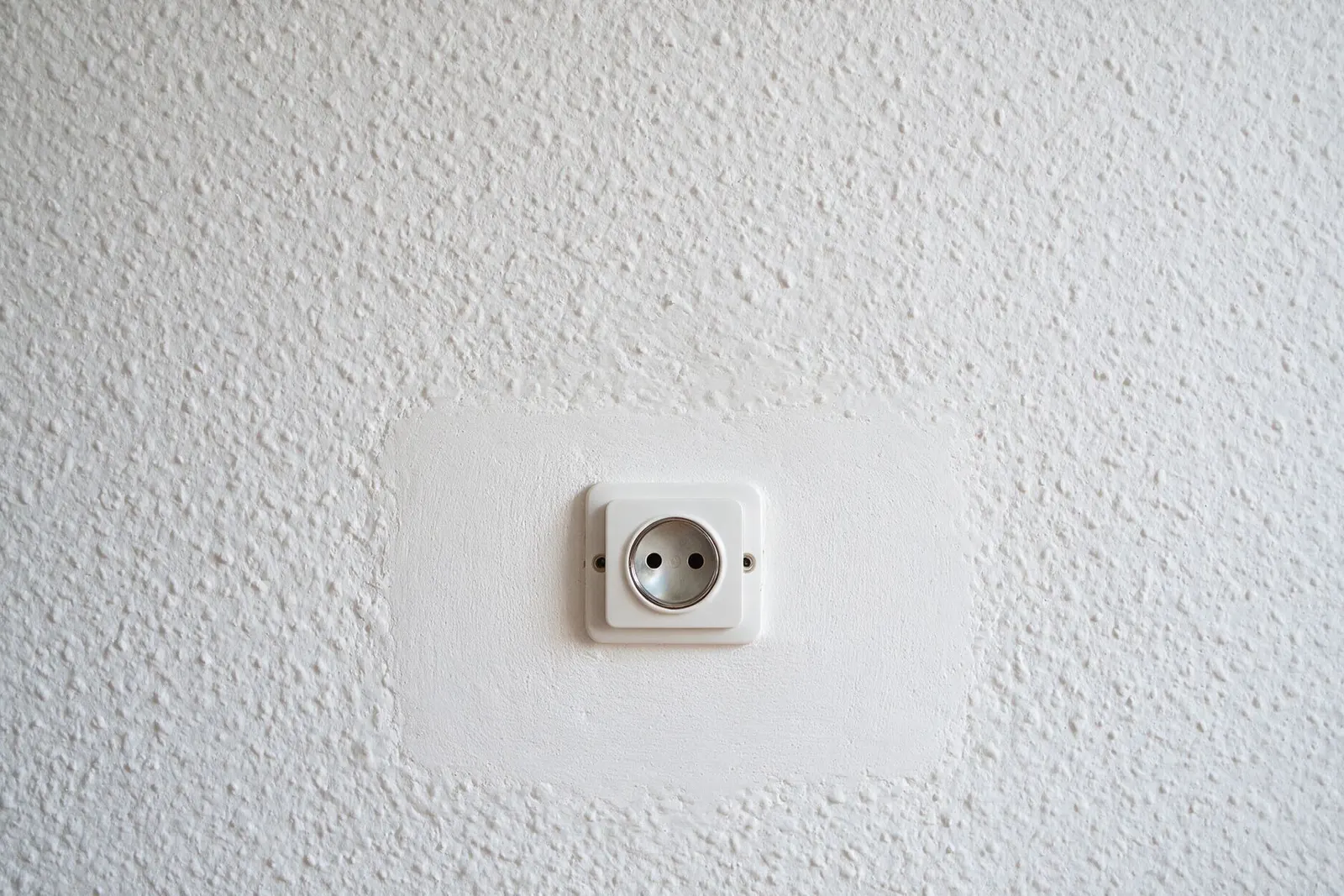 Pared con gotelé y un parche visible alrededor de un enchufe nuevo
