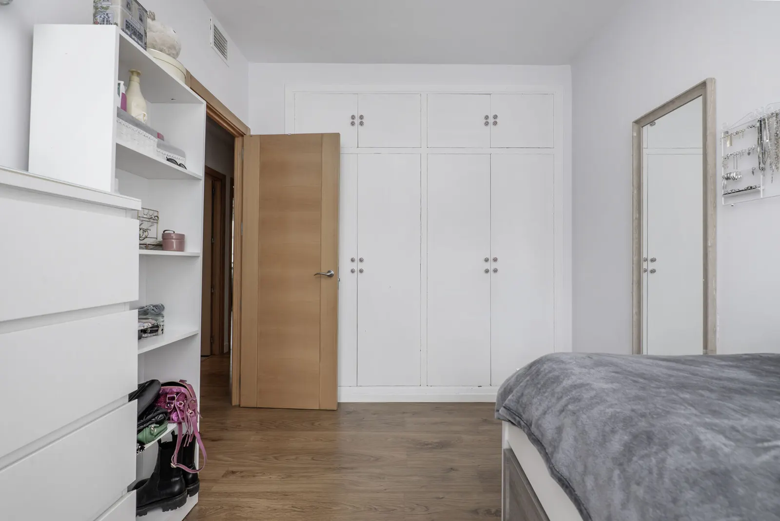 Dormitorio con armario empotrado de puertas blancas con molduras y suelo de madera