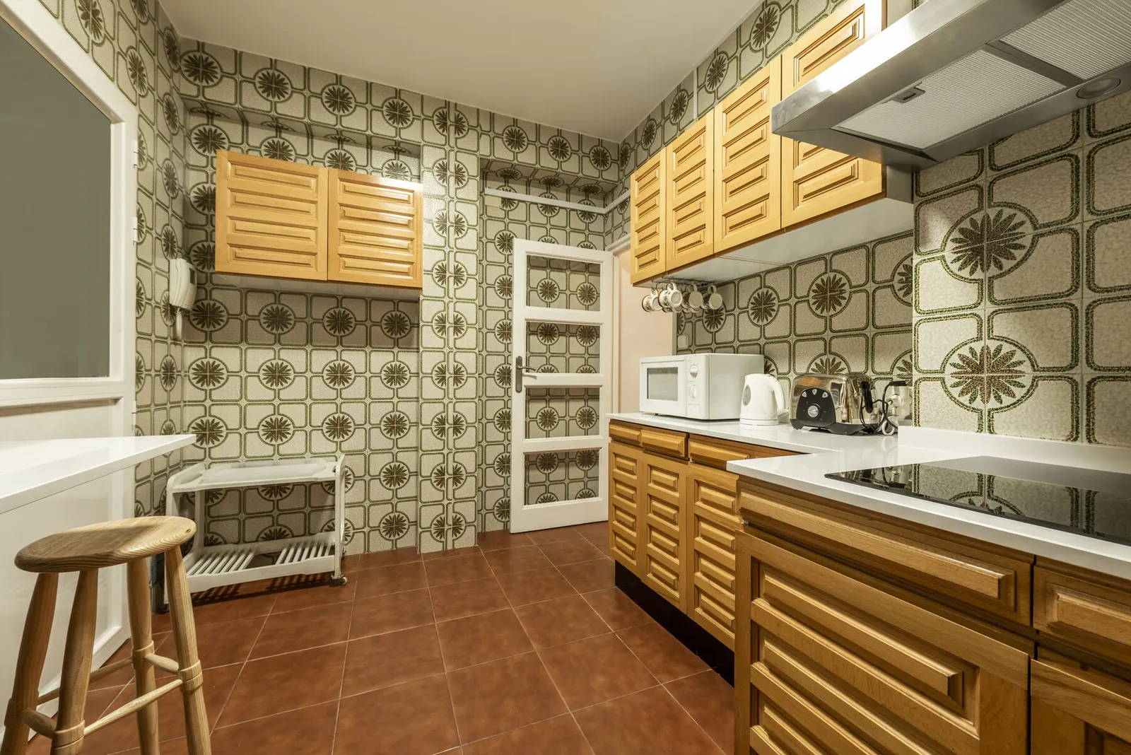 Cocina de los años noventa con muebles de madera barnizada, azulejos de dibujo y suelo de barro