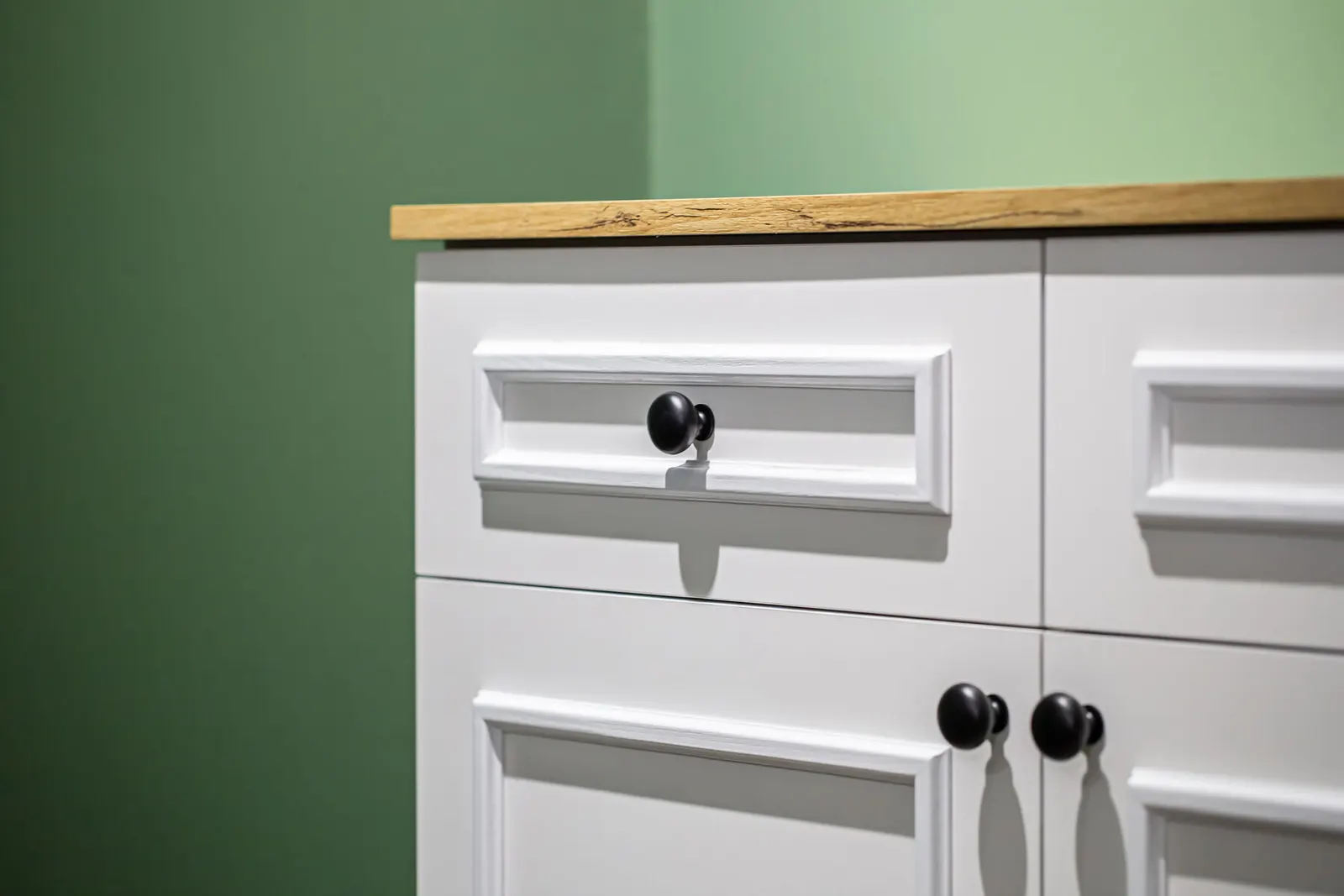 Mueble blanco lacado con cajones y puertas de cuarterones, pomos negros y encimera de madera