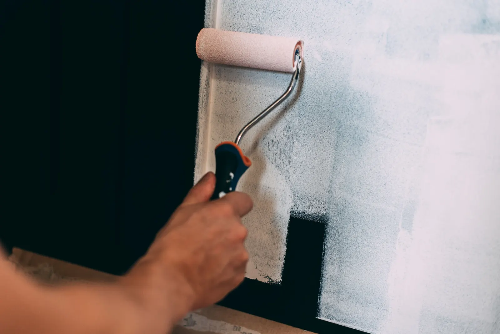 Rodillo aplicando pintura blanca sobre una pared lisa de color oscuro