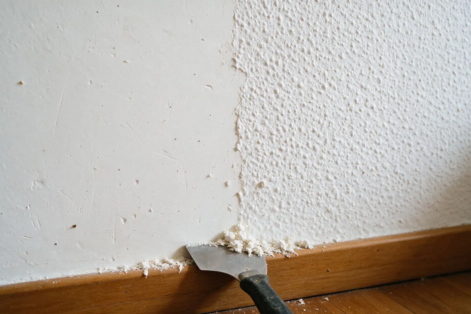 Pared con la mitad del gotelé raspado y la otra mitad todavía con textura, con una rasqueta junto al rodapié