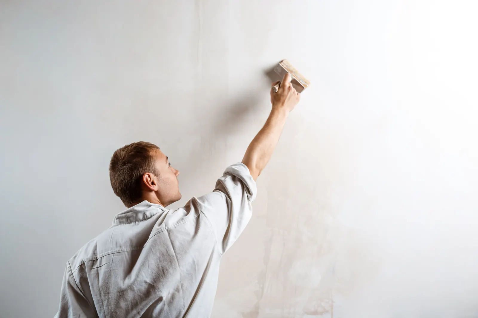 Pintor aplicando pintura blanca con una brocha ancha sobre una pared